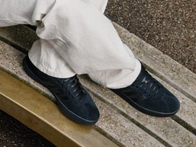 The image shows a pair of black leather shoes on a granite surface, with a white pant leg visible above them.