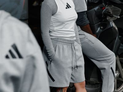 The image shows a person wearing an Adidas athletic outfit, including a white shirt and gray sweatpants, standing in front of a dark background.