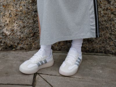 The image shows a person's lower body wearing gray pants and white sneakers standing on a concrete surface with a textured background.