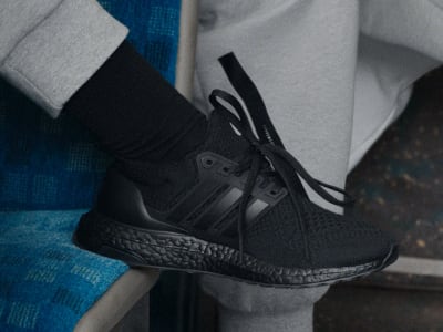 A close-up view of a person's foot wearing a black athletic shoe with laces against a blurred background of various fabrics.