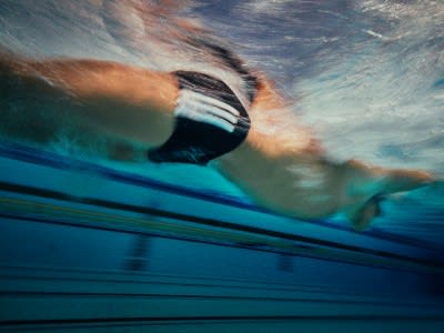 A blurred, underwater view of a person swimming, with the surface of the water and the sky visible in the background.