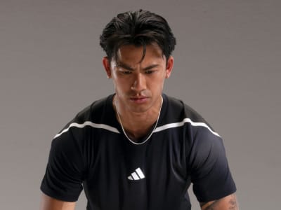 A man wearing a black Adidas sports jersey stands against a plain gray background, his expression serious and focused.