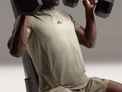 A person wearing a beige athletic shirt is lifting weights in a dimly lit room.