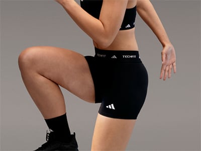 The image shows a person wearing black athletic clothing, including shorts and socks, posing against a plain gray background.