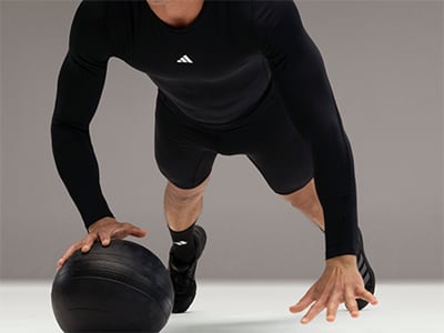 A person in black athletic clothing is crouched down, holding a black helmet in their hands.