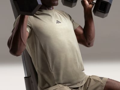 A person wearing a light-colored athletic shirt is lifting weights in a dimly lit room.