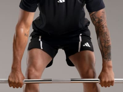 A person wearing black athletic clothing is gripping a metal bar, showcasing their muscular arms and torso against a plain background.