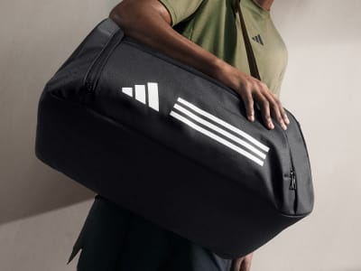 A person holding a black and white sports bag with the Adidas logo visible.