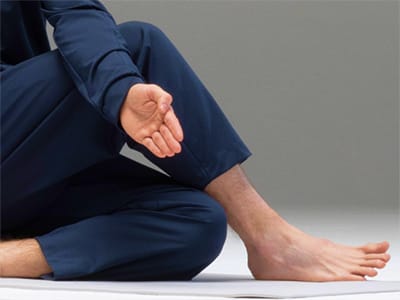 A person in a navy blue suit is sitting on the floor, with their hands resting on their knees and their bare feet visible.