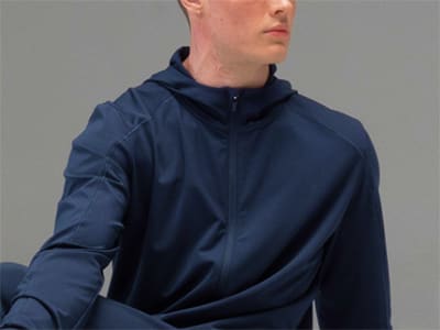 A person wearing a navy blue hooded jacket stands against a plain gray background.