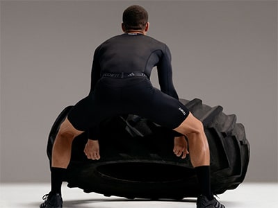 A person in a black bodysuit is sitting on a large, futuristic-looking vehicle against a plain gray background.