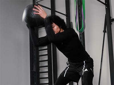 A person in a black outfit is leaning against a metal frame structure in a dimly lit room.
