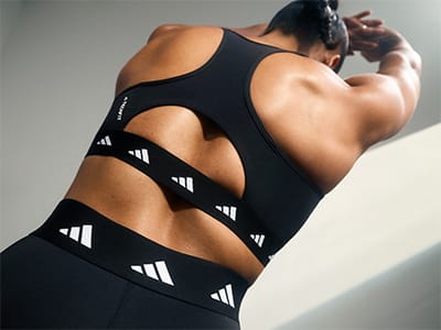 The image shows the back of a person wearing a black athletic top with white stripes, highlighting their muscular physique against a plain background.