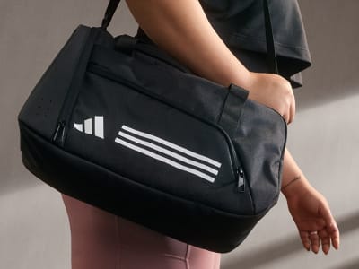 A black sports bag with the Adidas logo is being held by a person's hand against a plain background.