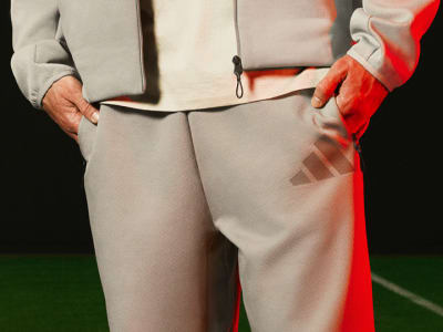 The image shows a person wearing a gray suit and a red scarf, standing on a green surface against a dark background.