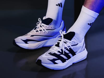 The image shows a pair of white and black athletic shoes with laces, set against a dark background.