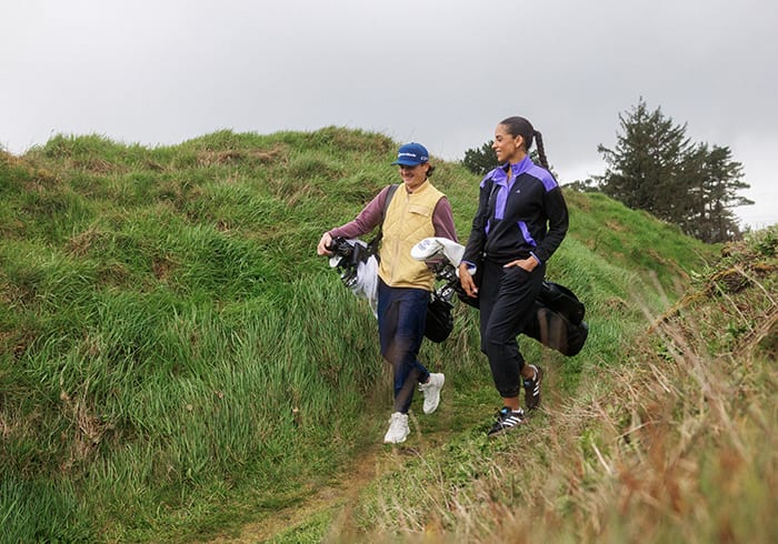 Man and woman walk together with their golf bags on a golf course.