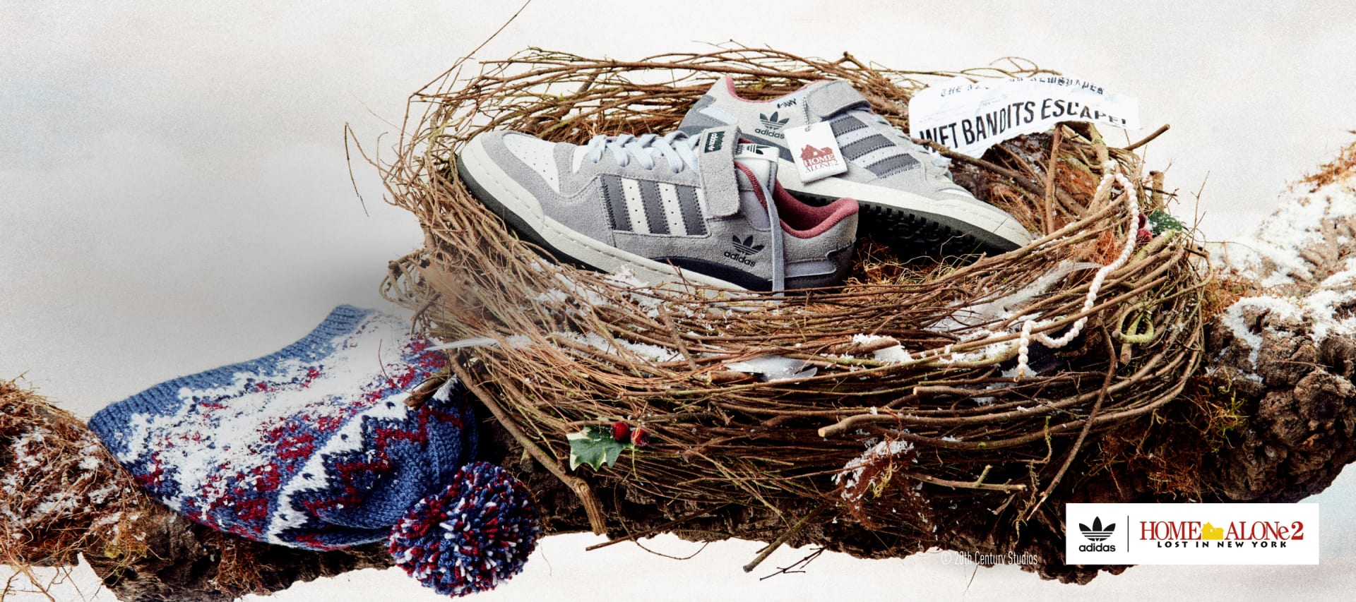 A pair of Forum Low Home Alone sneakers lie in a bird's nest on a snow-covered branch. Kevin's classic bobble hat lies next to it.