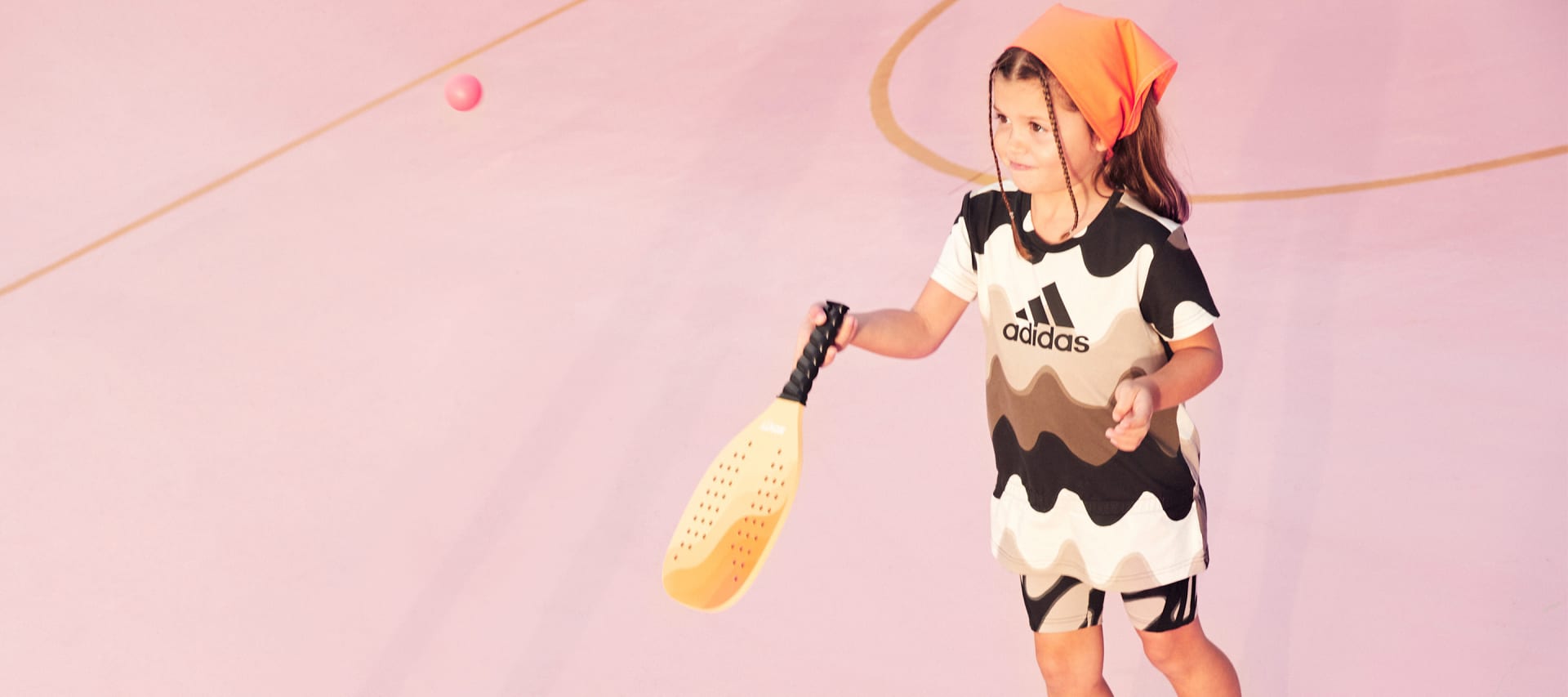 Little kid playing with a bat and ball wearing the adidas x marimekko collection.