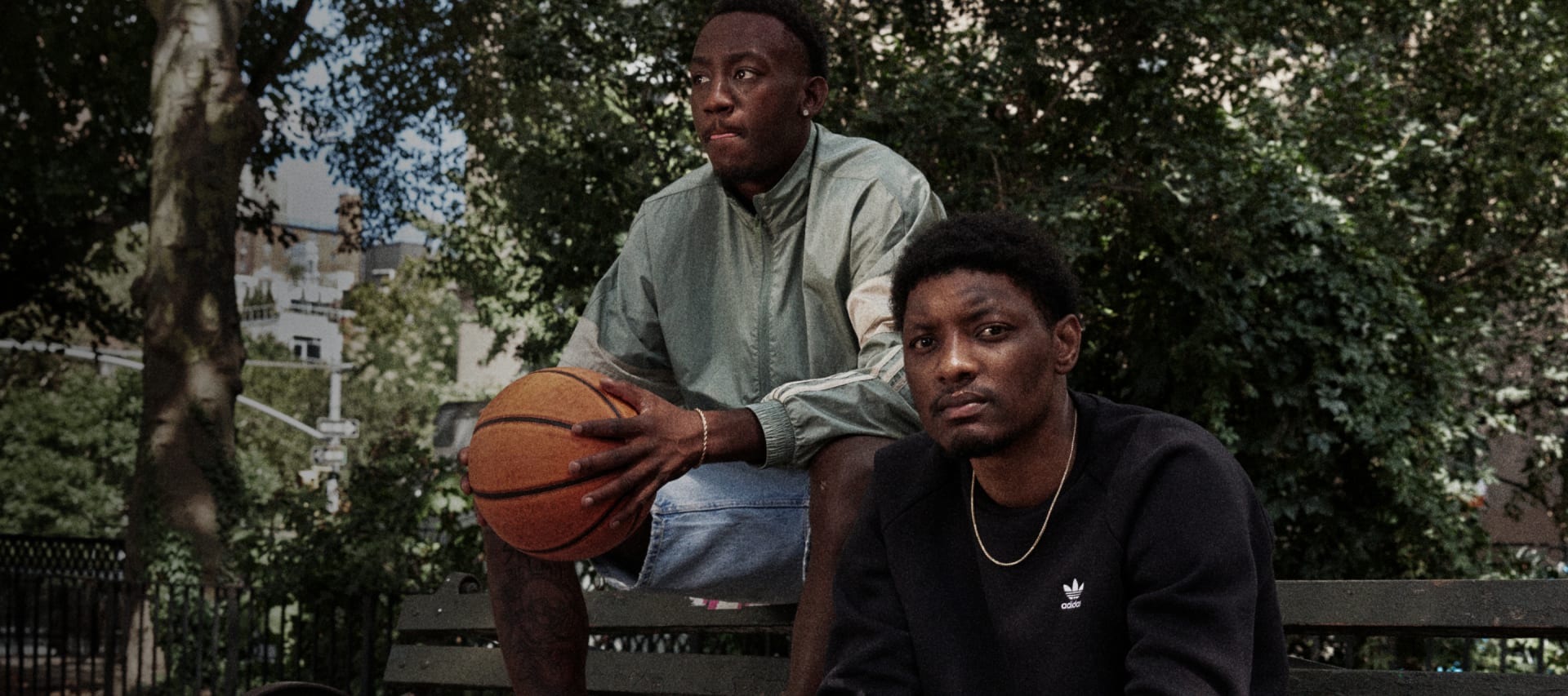 Two sitting men look to camera, one holding basketball