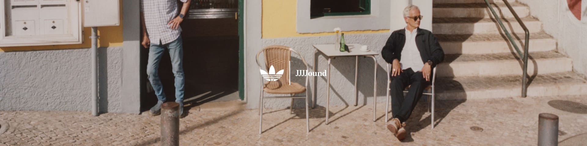 José Mourinho sits outside a café on a cobblestone street wearing the latest adidas Originals x JJJJound collection.