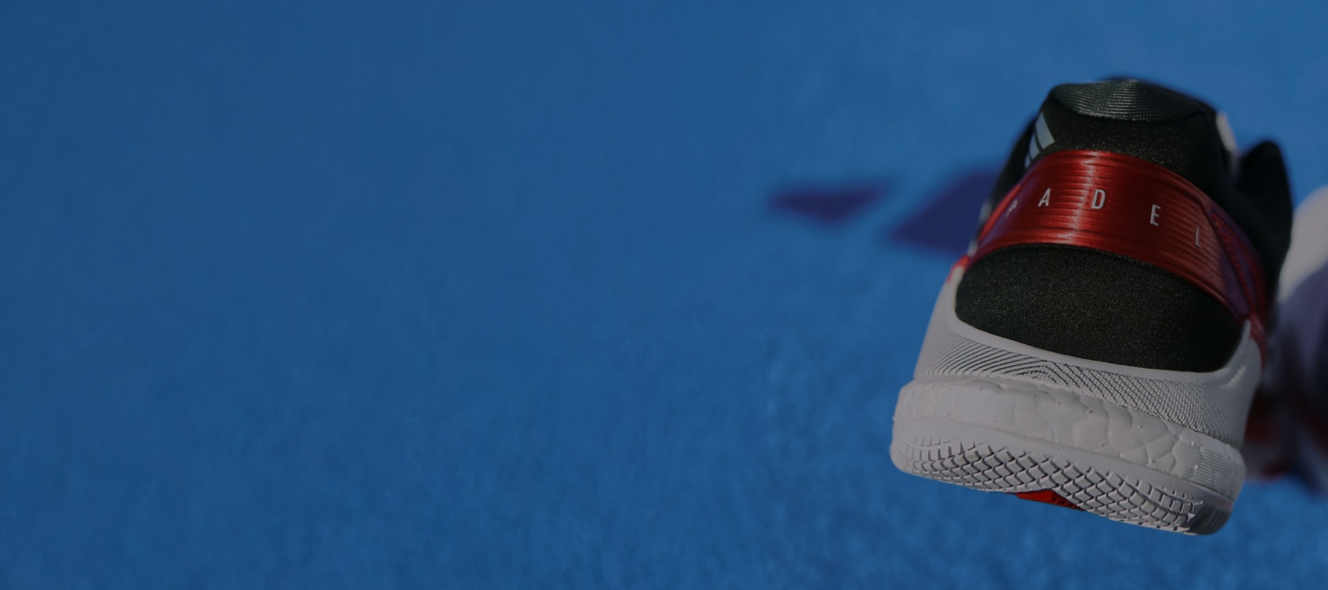 A close-up view of a red and white athletic shoe against a vibrant blue background.