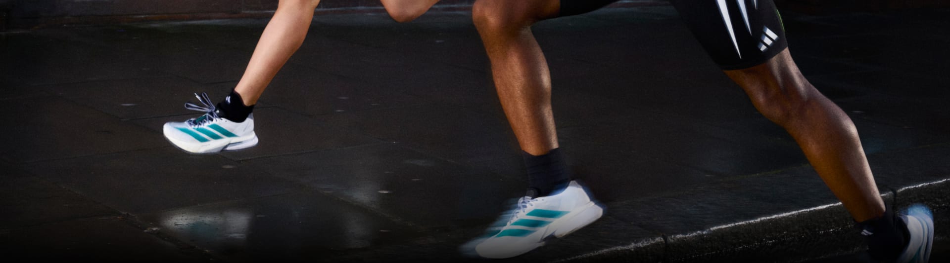 A woman and a man run down an urban street wearing the new Adizero Boston 13, as well as adidas shorts and tops.