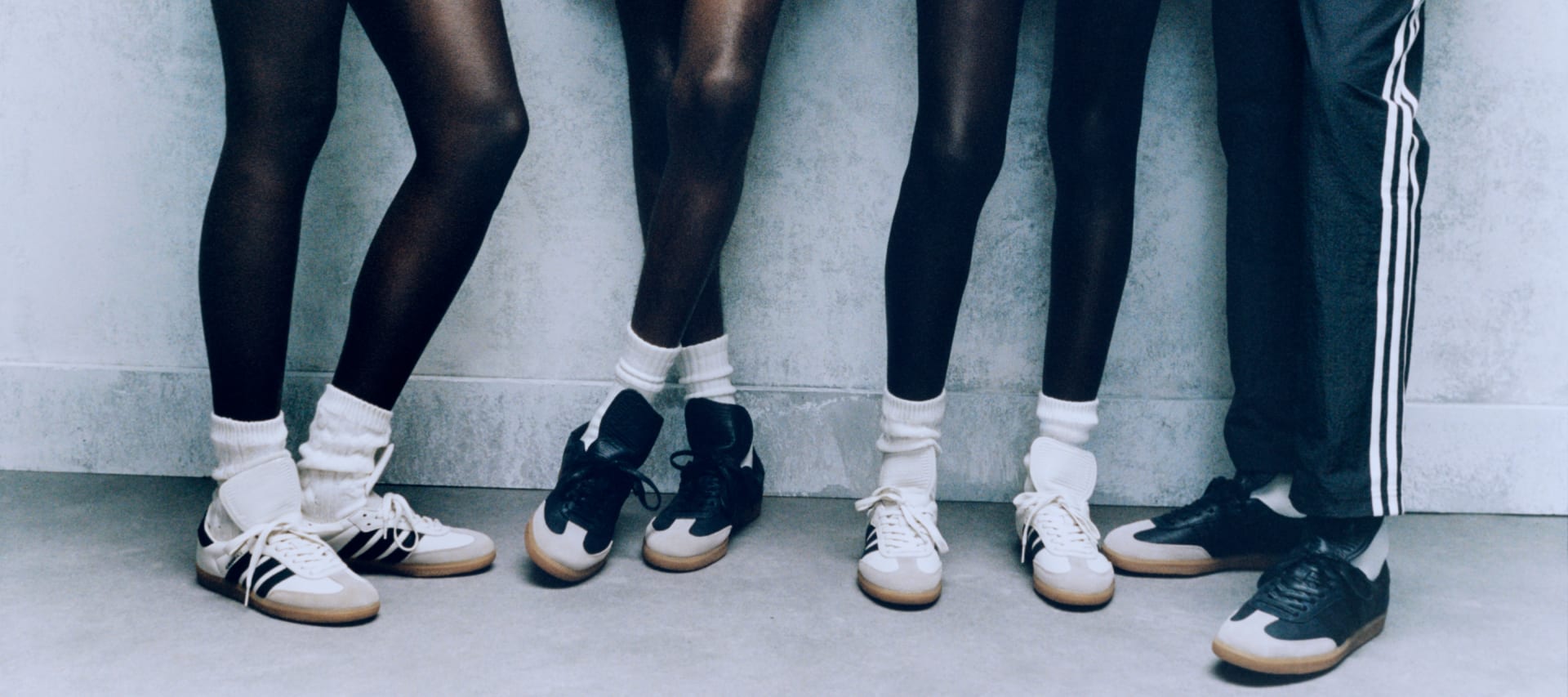 Models stand against wall wearing Samba sneakers