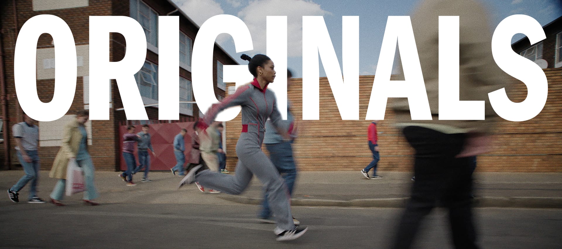 A person runs through an industrial setting, wearing adidas Originals.