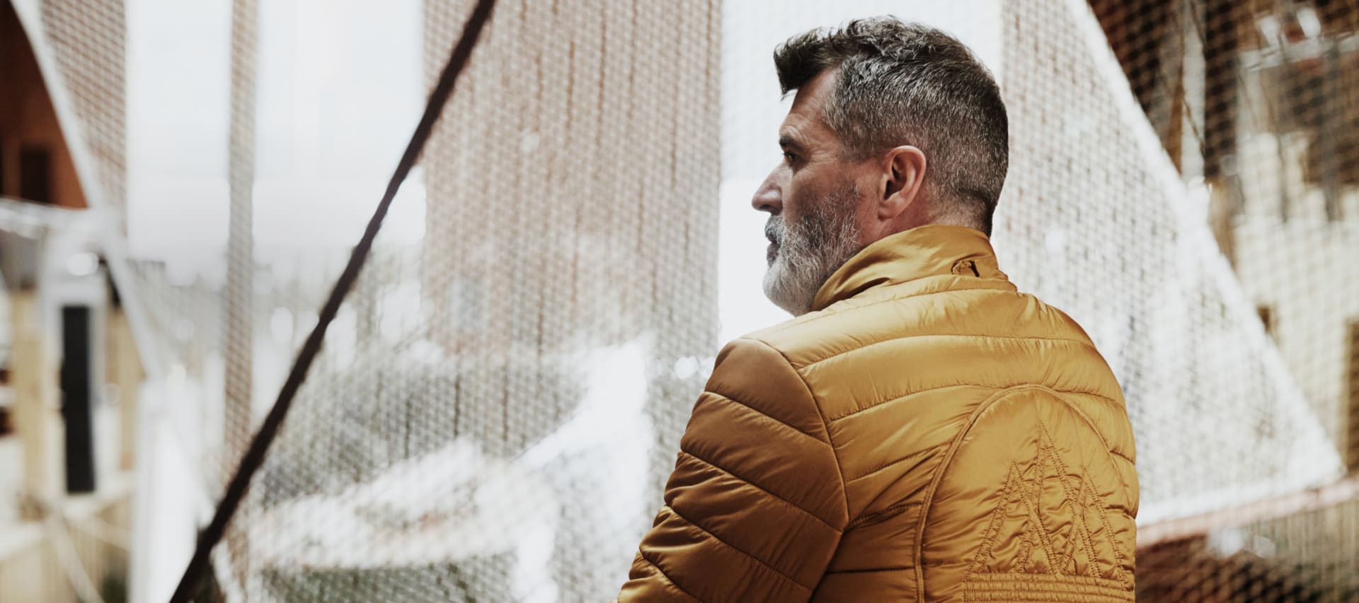 Roy Keane looks out of a window while wearing a yellow adidas Spezial puffer jacket.