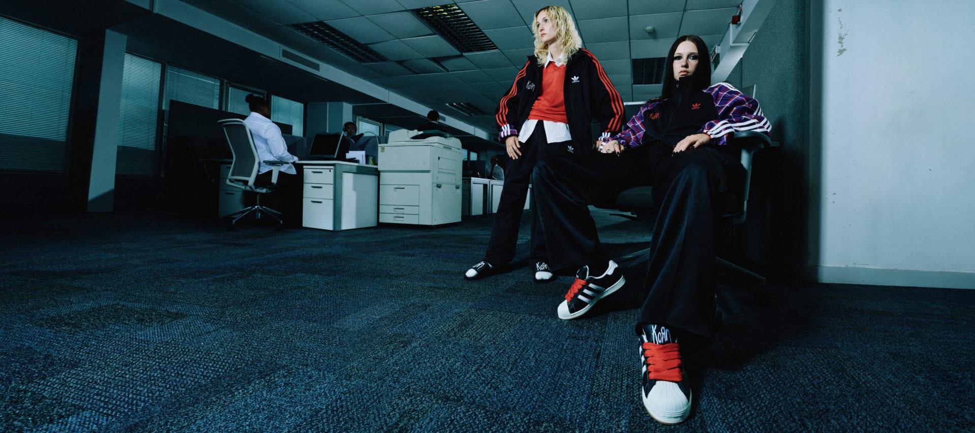 Two girls sitting in an office environment wearing the adidas Originals x KoRn collection.
