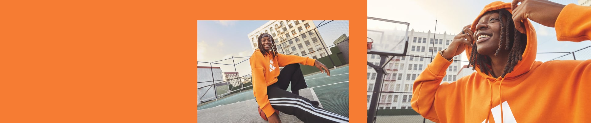 A woman sits on a basketball court, her back to the camera. She wears a orange adidas hoody and black adidas bottoms.