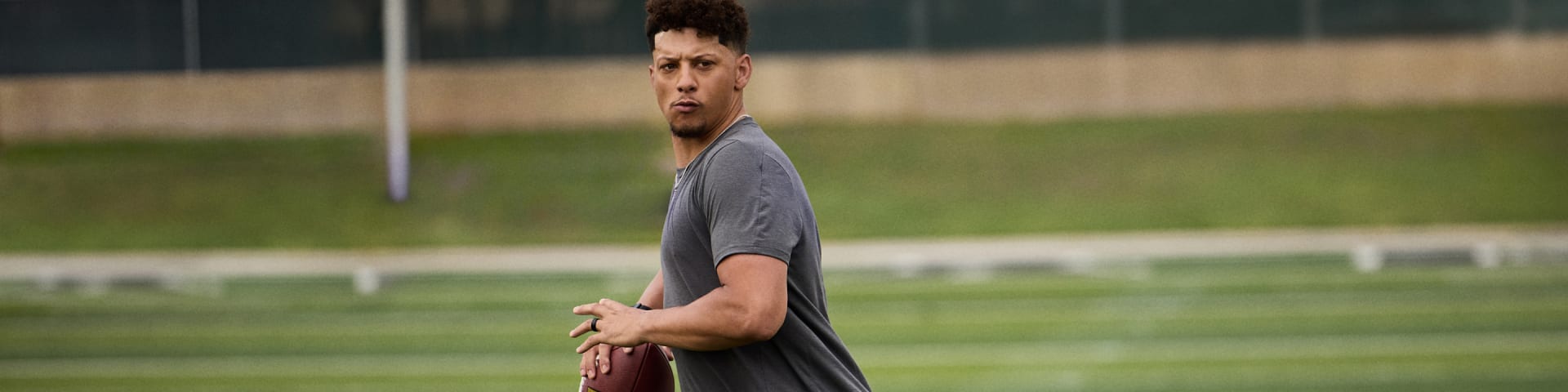 A young man with a serious expression stands on a grassy field, holding a football in his hands.