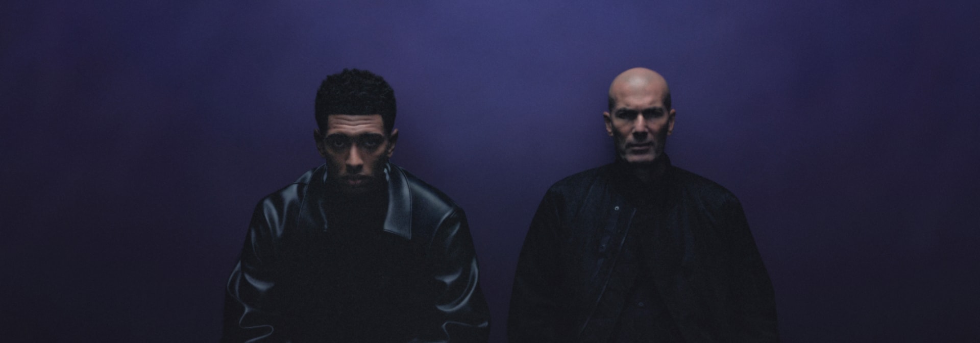 Jude Bellingham and Zinedine Zidane pose in front of a purple wall dressed from head to toe in black Y-3 apparel.