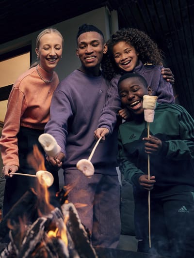 Image of a man, woman and kid wearing adidas tracksuits and roasting marshmallows.