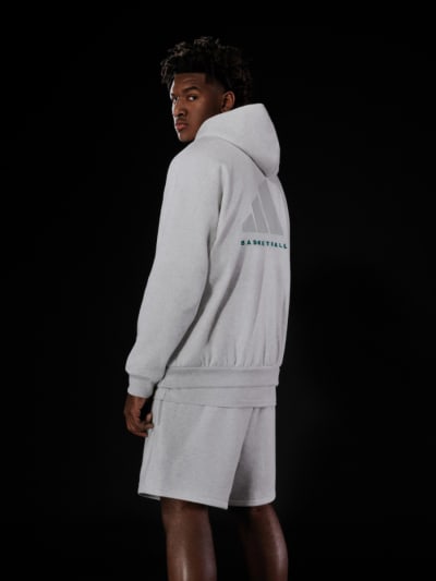 Model wearing grey hoodie and shorts looks back over shoulder.