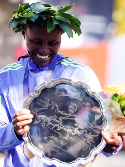 A smiling person wearing a blue and white striped shirt and a wreath of leaves on their head, holding a decorative plate with a celestial design.