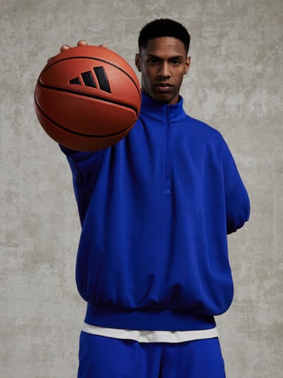 A man in a blue sweatshirt confidently holds a basketball, facing camera.