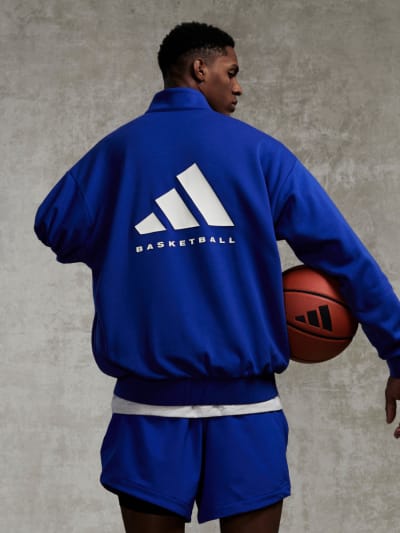 An adidas basketball player in a blue sweatshirt and shorts, holding a basketball.
