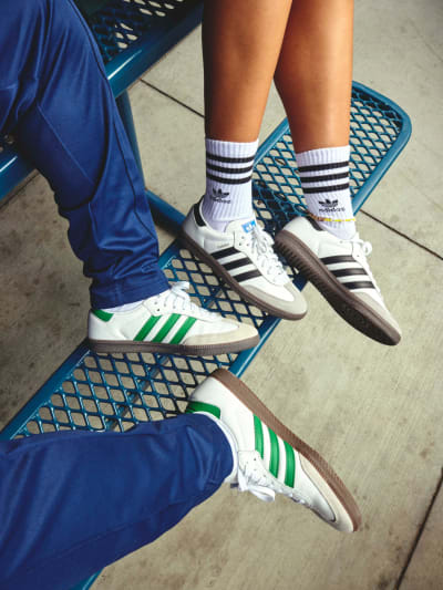 The image shows a person's legs and feet wearing Adidas sneakers and striped socks, standing on a blue and white metal bench or seat.