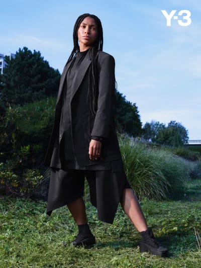 A woman with black braids wears all-black Y-3 apparel while posing in nature.