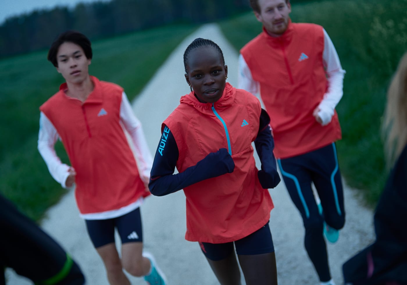 Peres Jepchirchir and other female runners running outside wearing Adizero running apparel, red vests and dark shorts