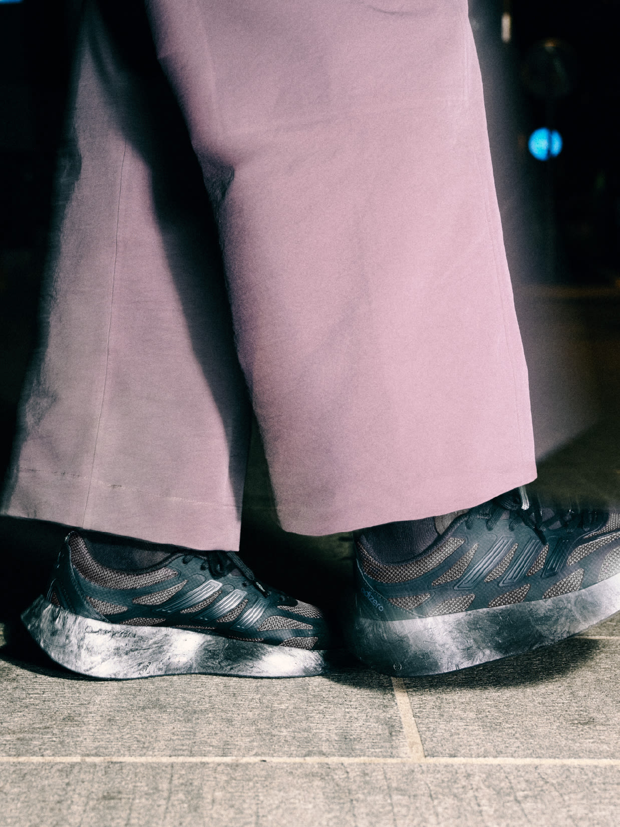 The image shows a person's lower body wearing a pink skirt and a pair of patterned rain boots standing on a tiled floor.