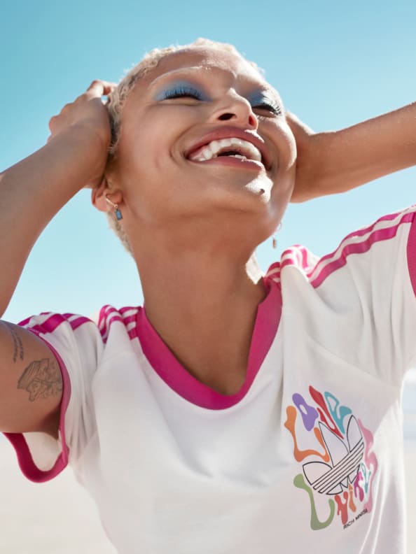 A female model laughs in a white and pink t-shirt from the adidas x Rich Mnisi Pride Collection.