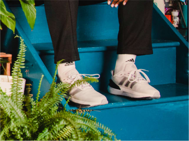 Close crop of adidas sneakers, shown on model sitting on a set of stairs.