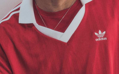 Close-up of a red Adidas shirt with a white collar and sleeve stripes.