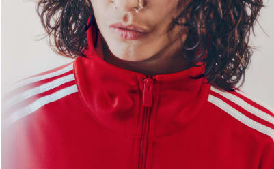 A man with black hair wearing a red adicolor tracksuit pictured from the neck up.