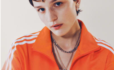 A woman with short brown hair wearing an orange adicolor tracksuit pictured from the neck up.