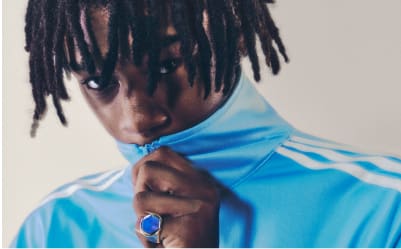 A man with black hair wearing a light blue adicolor tracksuit pictured from the neck up.