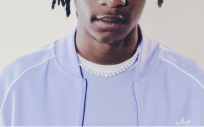A man with black hair wearing a lavender adicolor tracksuit pictured from the neck up.